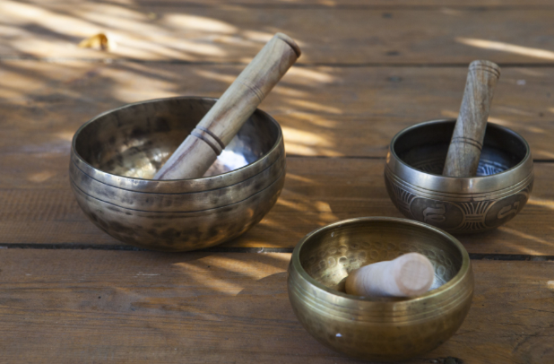 三個不同尺寸的銅製頌缽與木製缽槌，被放置在戶外木桌上