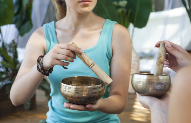 一位穿著藍綠色背心的女性正在操作銅製頌缽，另一人也持有頌缽