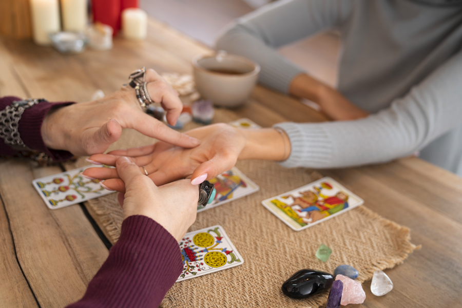 一位戴著戒指和手鐲的人正在閱讀另一位手上客人的手相，桌面擺有塔羅牌、水晶和一杯茶
