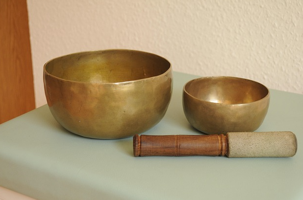 兩個不同大小的銅製頌缽和一個木柄缽槌放在淺綠色的表面上