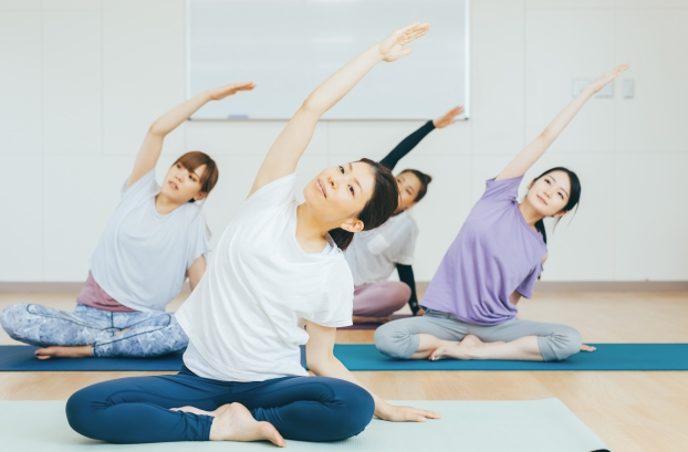 幾位女性在明亮的房間裡，坐在瑜珈墊上，一起進行側彎伸展的瑜珈動作