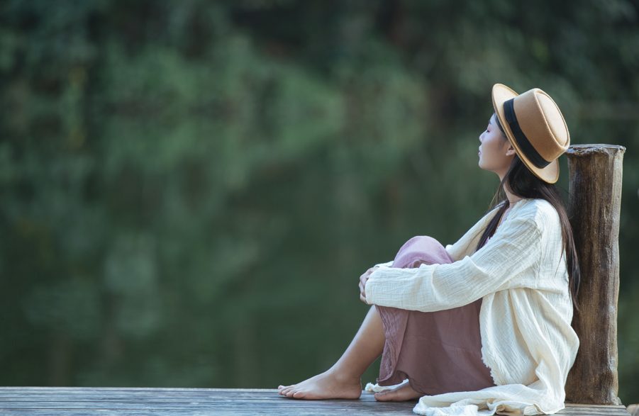 女子坐在木棧道邊緣看著湖面/戴著草帽沉思或放鬆/享受寧靜的自然風景/戶外冥想與心靈療癒