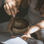 瑜伽服裝的女子坐在墊子上_進行聲音冥想或脈輪平衡_專注於頌缽發出的振動