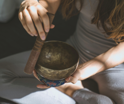 瑜伽服裝的女子坐在墊子上_進行聲音冥想或脈輪平衡_專注於頌缽發出的振動