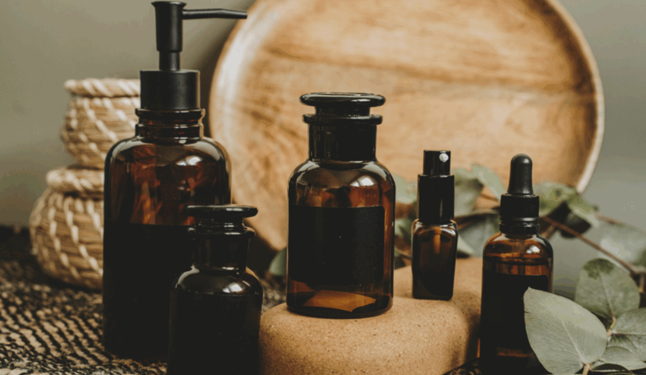 一系列深棕色精油瓶，擺在木紋圓盤和編織墊前，周圍裝飾有綠色尤加利葉