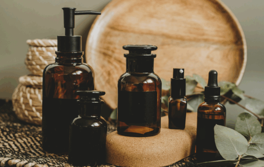 一系列深棕色精油瓶，擺在木紋圓盤和編織墊前，周圍裝飾有綠色尤加利葉