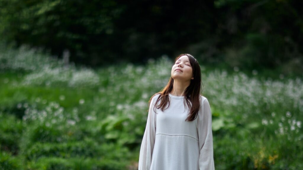 一位年輕女性在翠綠的森林背景中仰頭閉目深呼吸，享受大自然帶來的靜謐與紓壓時刻