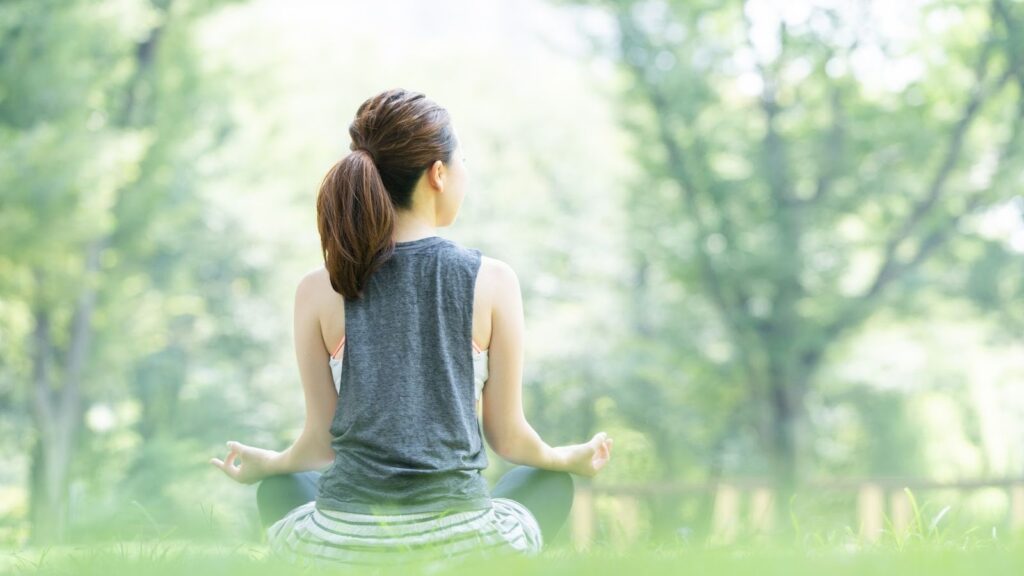 瑜伽練習者的背面視角，在公園綠地中採取盤腿坐姿並掐指捏印（Mudra），進行深度禪定。