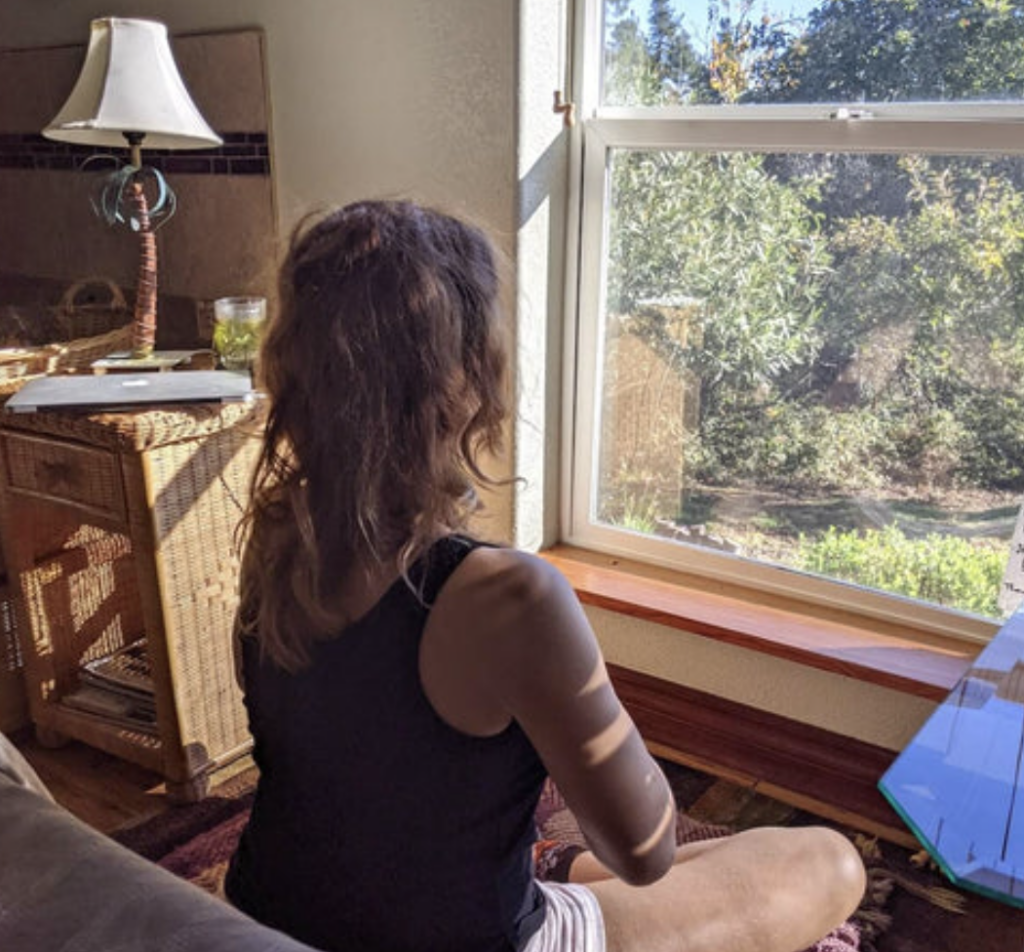 一名女子背對窗外自然光靜坐於室內，凝視窗景，呈現安靜獨處與自我沉澱的氛圍