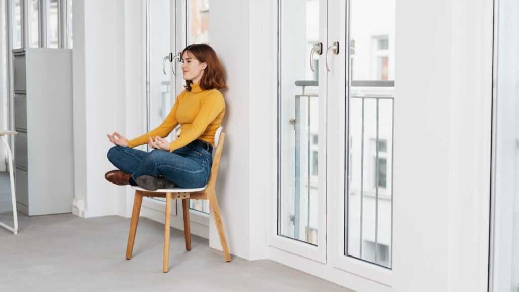 創意冥想場景：女性在辦公環境中坐在椅子上盤腿冥想，強調隨處皆可靜心與釋放壓力。