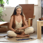 一名女子盤坐在溫暖的居家空間中靜心冥想，雙手輕放物件，營造放鬆而內在專注的氛圍