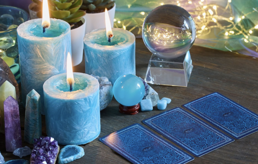 在木質桌面上，幾張塔羅牌呈扇形展開，牌面上顯示著「權杖四」與「力量」等經典圖樣；背景擺放著數顆粉晶、紫水晶等天然原石，以及一個裝有彩色小礦石的月亮形托盤，營造出神祕學與身心靈療癒的視覺氛圍