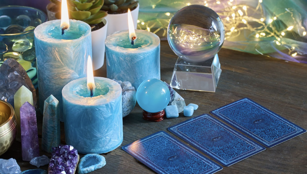 在木質桌面上，幾張塔羅牌呈扇形展開，牌面上顯示著「權杖四」與「力量」等經典圖樣；背景擺放著數顆粉晶、紫水晶等天然原石，以及一個裝有彩色小礦石的月亮形托盤，營造出神祕學與身心靈療癒的視覺氛圍