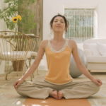 一位女性在充滿自然光的溫馨客廳地板上盤腿冥想，背景有白色沙發與綠意植栽。