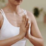 穿著白色運動內衣的女性於室內合掌冥想，動作端正且神情專注，展現內在平靜