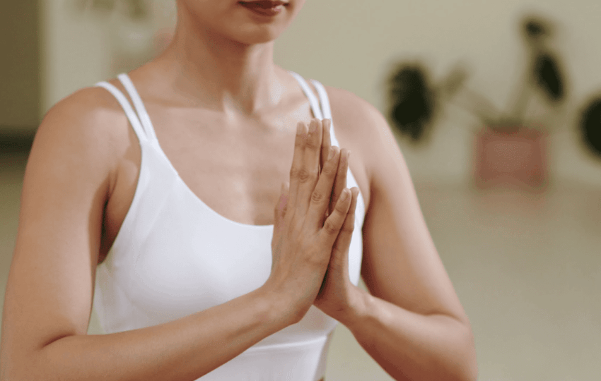 穿著白色運動內衣的女性於室內合掌冥想，動作端正且神情專注，展現內在平靜