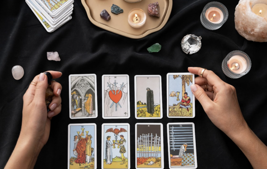 一雙手正在黑色桌面上進行塔羅牌占卜，桌上擺放著多張塔羅牌、水晶原礦、透明球體及數盞點燃的蠟燭