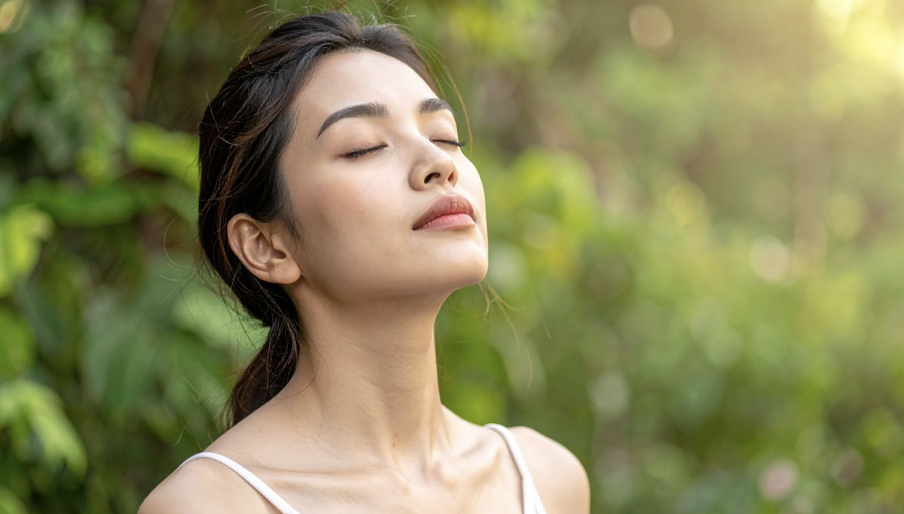 一名年輕女性在戶外綠意盎然的背景下閉目養神，微風吹拂，呈現出與大自然連結的寧靜感