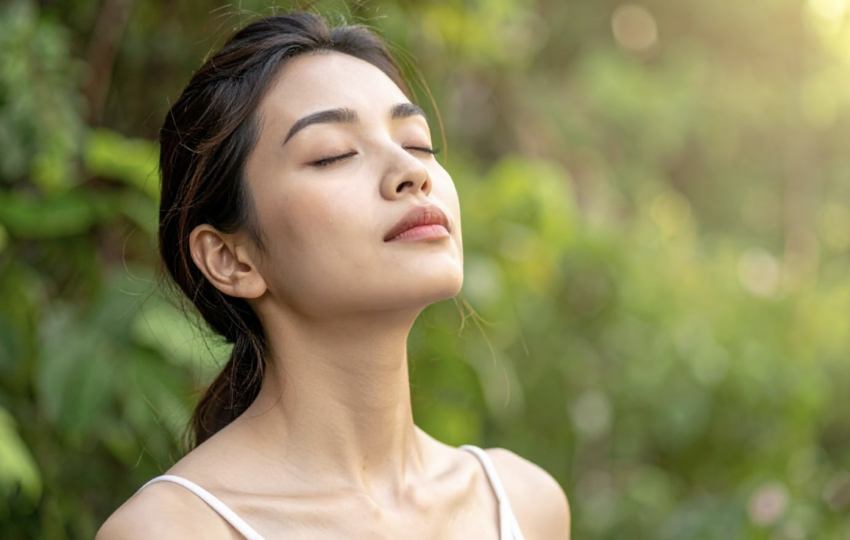 一名年輕女性在戶外綠意盎然的背景下閉目養神，微風吹拂，呈現出與大自然連結的寧靜感
