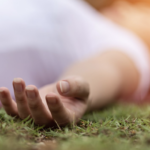 一個人平躺在翠綠草地上的特寫，手掌自然放鬆張開，展現與大自然連結的靜謐時刻。