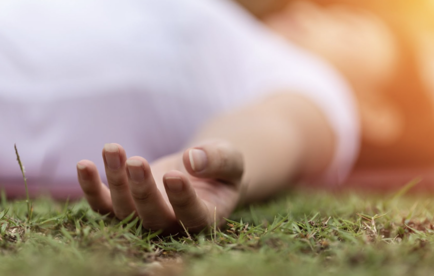 一個人平躺在翠綠草地上的特寫，手掌自然放鬆張開，展現與大自然連結的靜謐時刻。