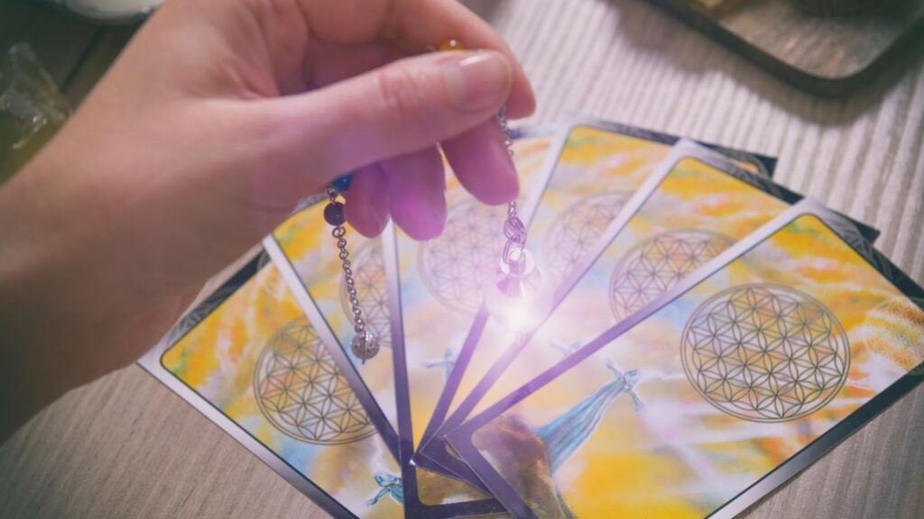 手持水晶靈擺在五張扇形展開的塔羅牌上方感應，水晶發出微弱光芒，適合用於能量療癒或占卜情境