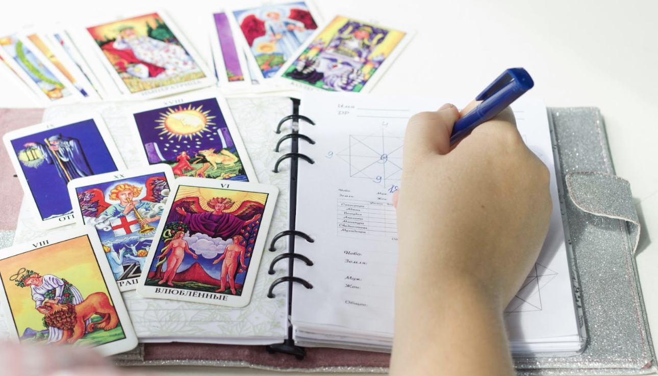 塔羅牌占卜師在筆記本上記錄占卜結果與星盤分析] 敘述： 塔羅牌陣與手寫筆記的交織，是與潛意識對話的過程。透過詳細的記錄，將神祕學符號轉化為生活指引