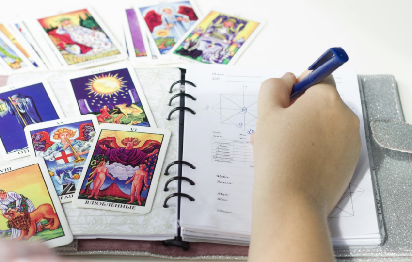 塔羅牌占卜師在筆記本上記錄占卜結果與星盤分析] 敘述： 塔羅牌陣與手寫筆記的交織，是與潛意識對話的過程。透過詳細的記錄，將神祕學符號轉化為生活指引