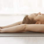 女子躺在瑜伽墊上進行深度放鬆與冥想伸展] 敘述： 靜心不一定要坐著，躺在墊上感受身體與大地的連結。藉由深呼吸，釋放堆積在肌肉裡的壓力，重拾內心的平靜。