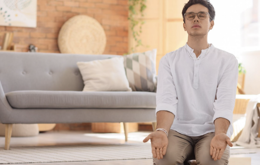 一名男子在客廳溫馨的環境中盤腿坐著進行冥想練習，雙手掌心向上，展現平靜與放鬆的身心狀態