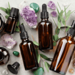 灰色石紋背景上散布著多瓶深色玻璃精油滴瓶、紫水晶與綠色礦石，並點飾著尤加利葉與點燃的蠟燭，營造芳香療法氛圍