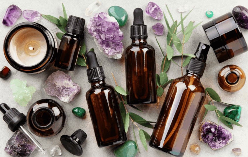 灰色石紋背景上散布著多瓶深色玻璃精油滴瓶、紫水晶與綠色礦石，並點飾著尤加利葉與點燃的蠟燭，營造芳香療法氛圍