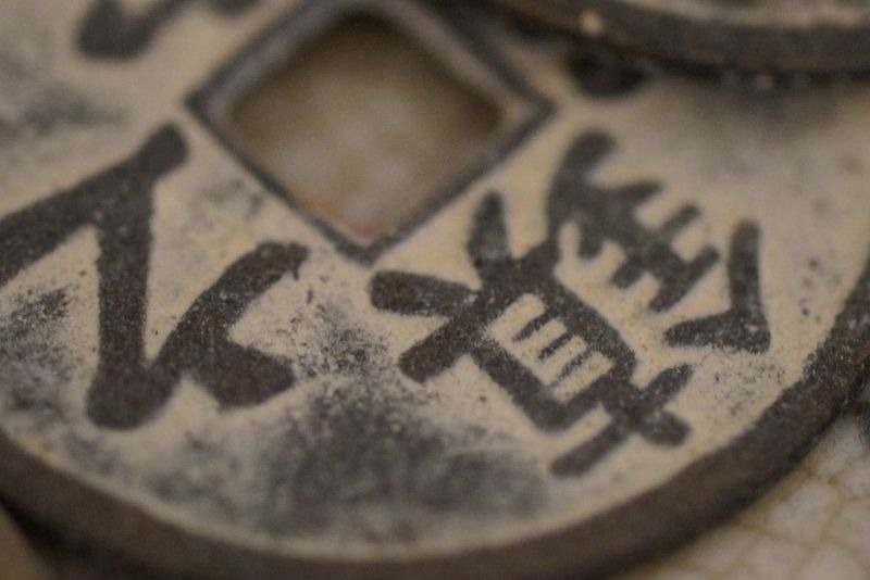 一枚帶有歲月痕跡的古代圓形方孔銅錢近距離特寫，硬幣表面文字斑駁且佈滿鐵鏽與泥土感，展現出古樸且沉重的歷史質感