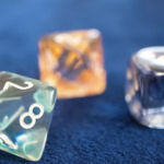 藍色絲絨背景上散落著三顆半透明且帶有光澤的占卜骰子，前景骰子清晰呈現數字 2、8、5，背景骰子則帶有柔和的橘色與紫色調