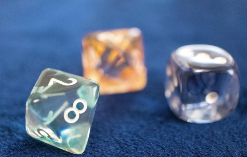 藍色絲絨背景上散落著三顆半透明且帶有光澤的占卜骰子，前景骰子清晰呈現數字 2、8、5，背景骰子則帶有柔和的橘色與紫色調