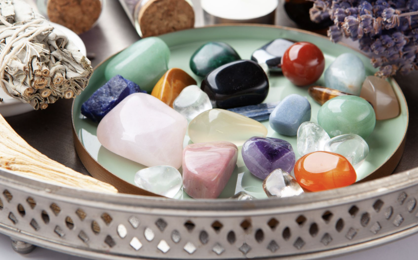 銀色托盤中擺放著各種色彩繽紛的拋光能量水晶原石，旁邊附有鼠尾草束與薰衣草。
