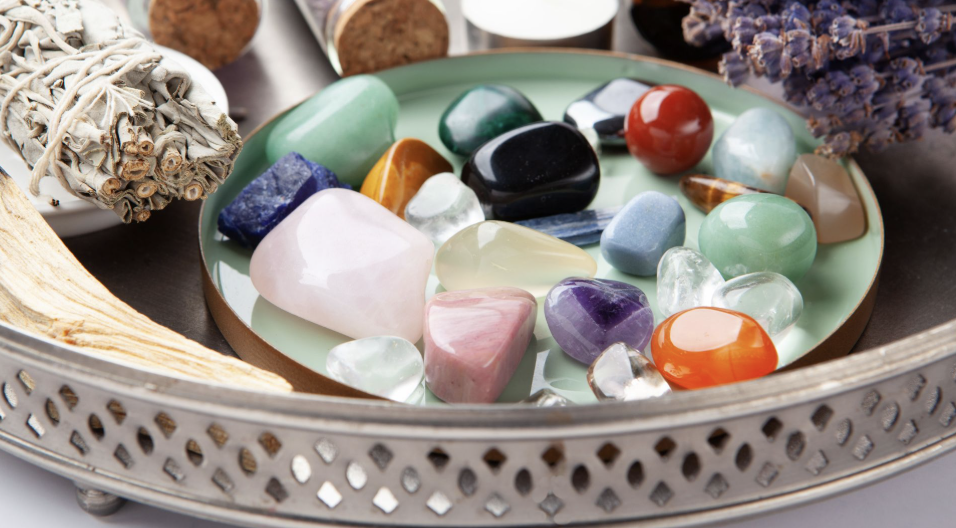銀色托盤中擺放著各種色彩繽紛的拋光能量水晶原石，旁邊附有鼠尾草束與薰衣草。