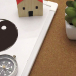 白板上繪製著太極圖案，旁邊放置指南針、迷你木屋模型與綠色小盆栽，象徵風水布局概念