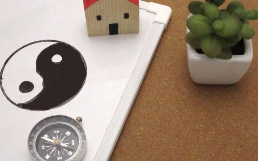 白板上繪製著太極圖案，旁邊放置指南針、迷你木屋模型與綠色小盆栽，象徵風水布局概念