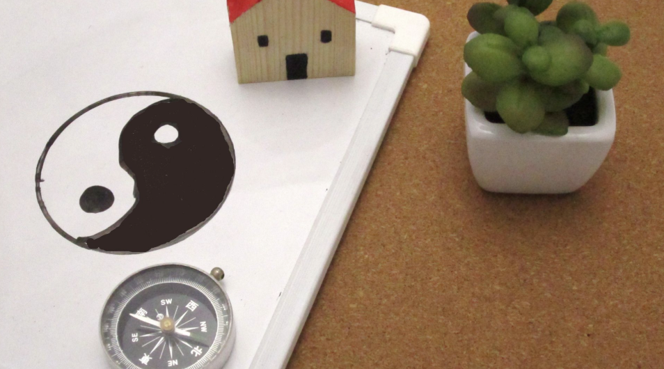 白板上繪製著太極圖案，旁邊放置指南針、迷你木屋模型與綠色小盆栽，象徵風水布局概念
